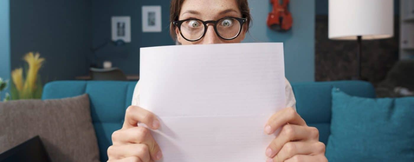 Shocked woman holding a sheet and staring with eyes wide open, expensive bills and debt concept