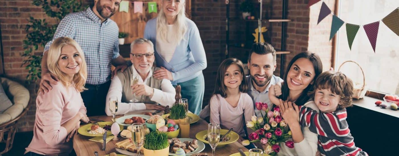 Close up photo of large company gathered family holiday sitting with flowers tulips champagne hugs toothy smiles easter eggs gladness decorations weekend vacation